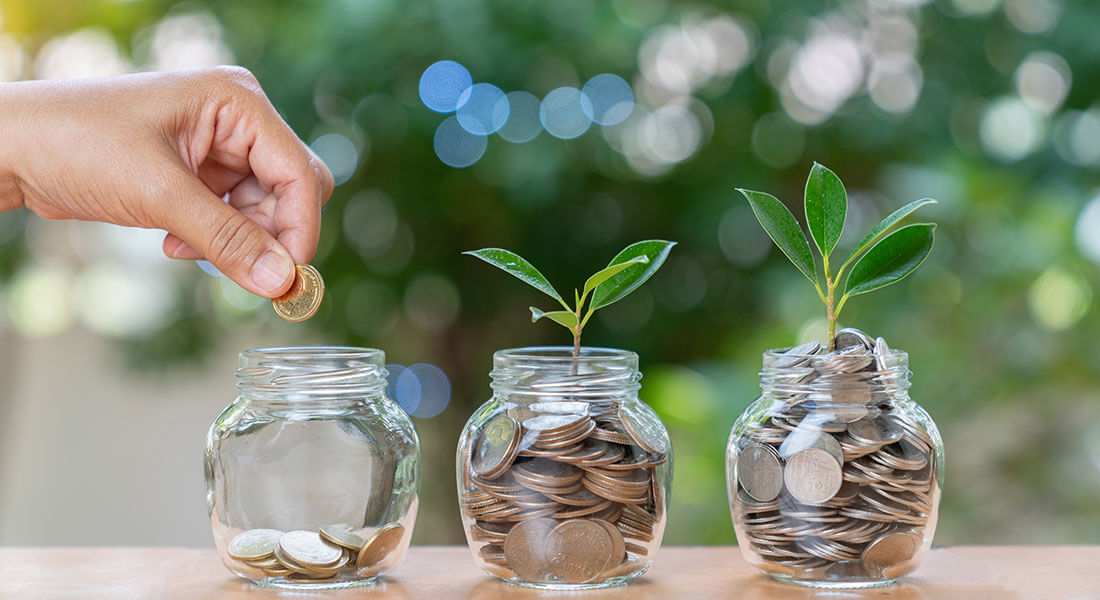 Hand dropping coin into investing glass jars